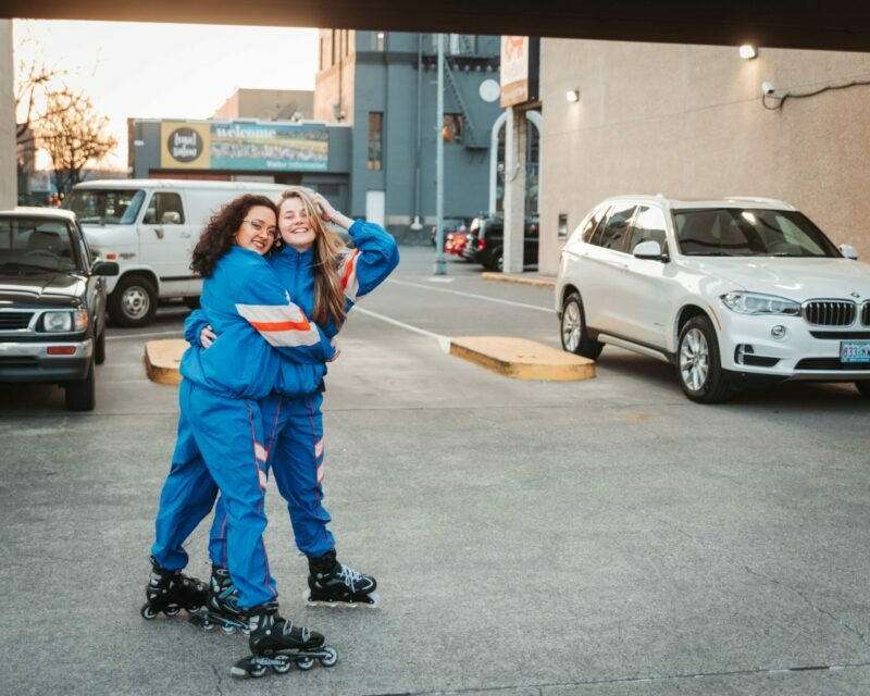Two rollerbladers in blue suits hug and smile at the camera in a parking lot in downtown Salem