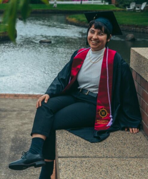 A recent graduate smiles off into the distance near the Mill Stream at Willamette University